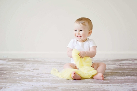 small baby sitting on the ground holding a yellow blanket