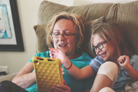 grandma and granddaughter sitting on a couch playing on a tablety